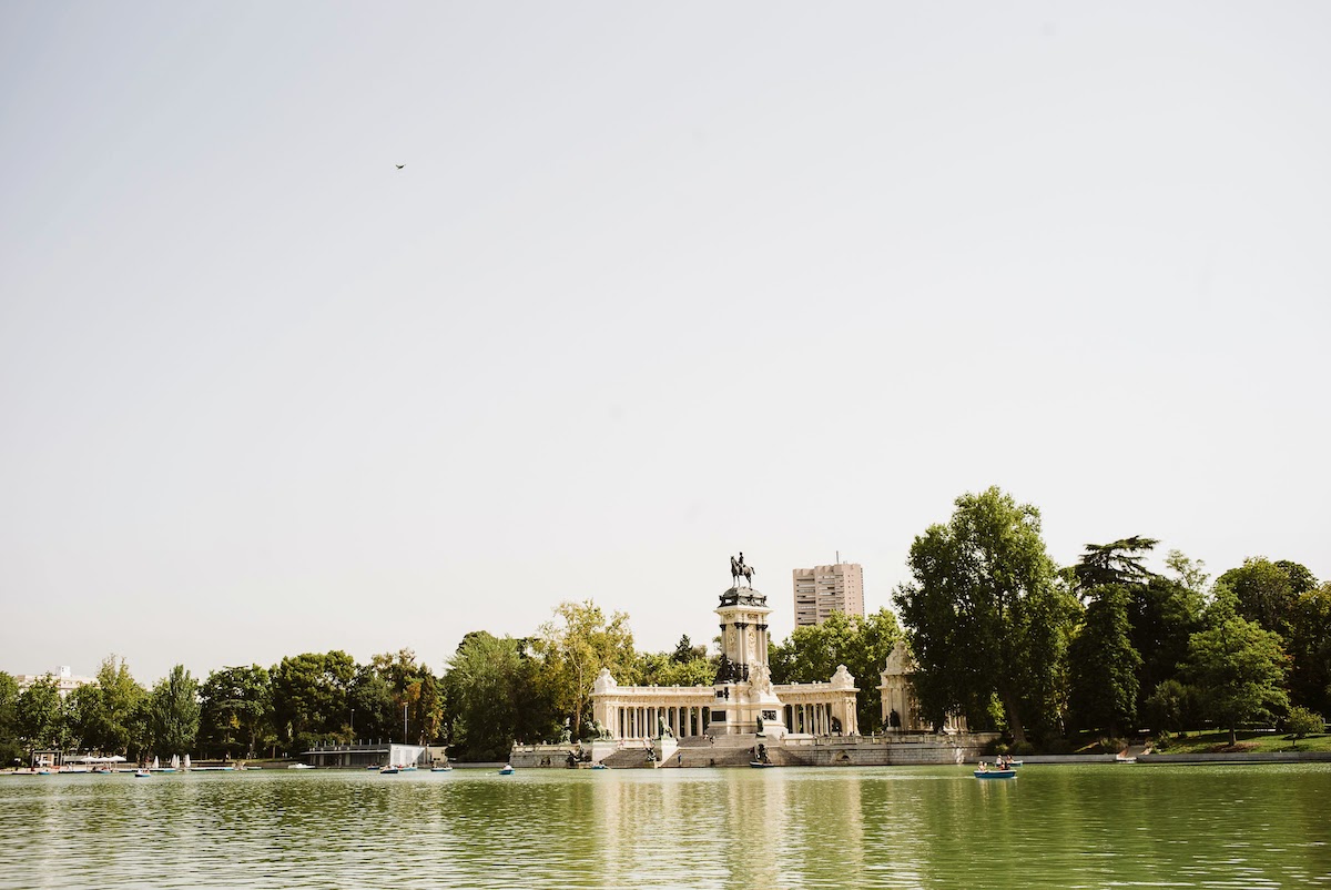Pequeños botes de remos en el lago del parque del Retiro de Madrid con un monumento visible al fondo.