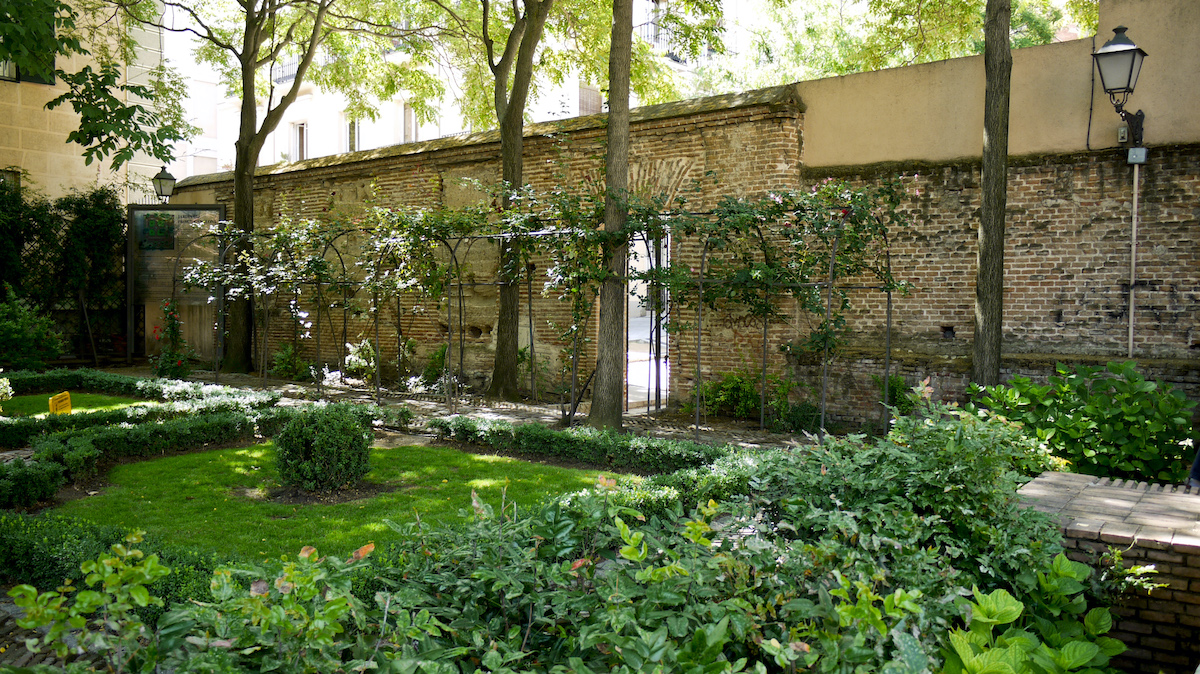 Hierba verde y plantas en un tranquilo jardín rodeado por un muro de piedra.