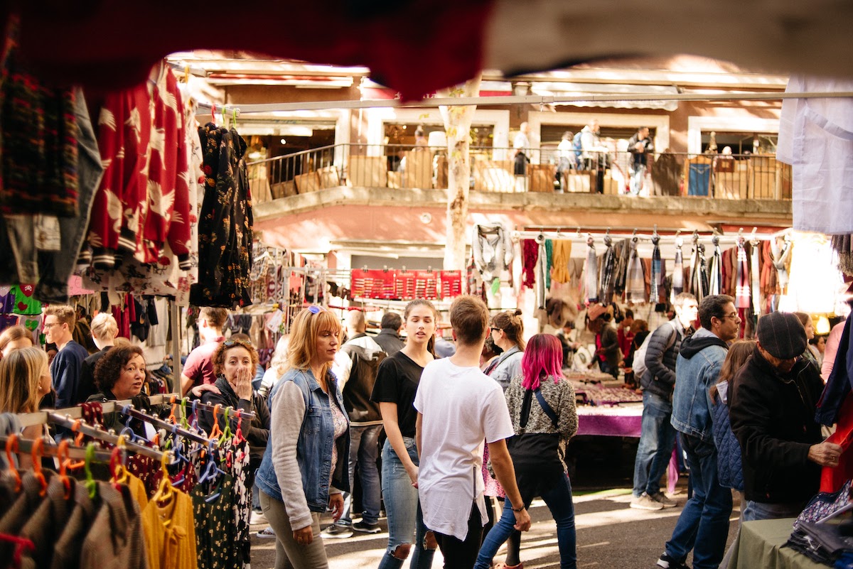 Multitud de personas caminando por puestos de ropa en un mercado de pulgas.