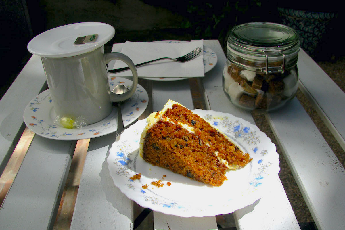 Rebanada de pastel de zanahoria junto a una taza de té y un bote de cristal con terrones de azúcar.