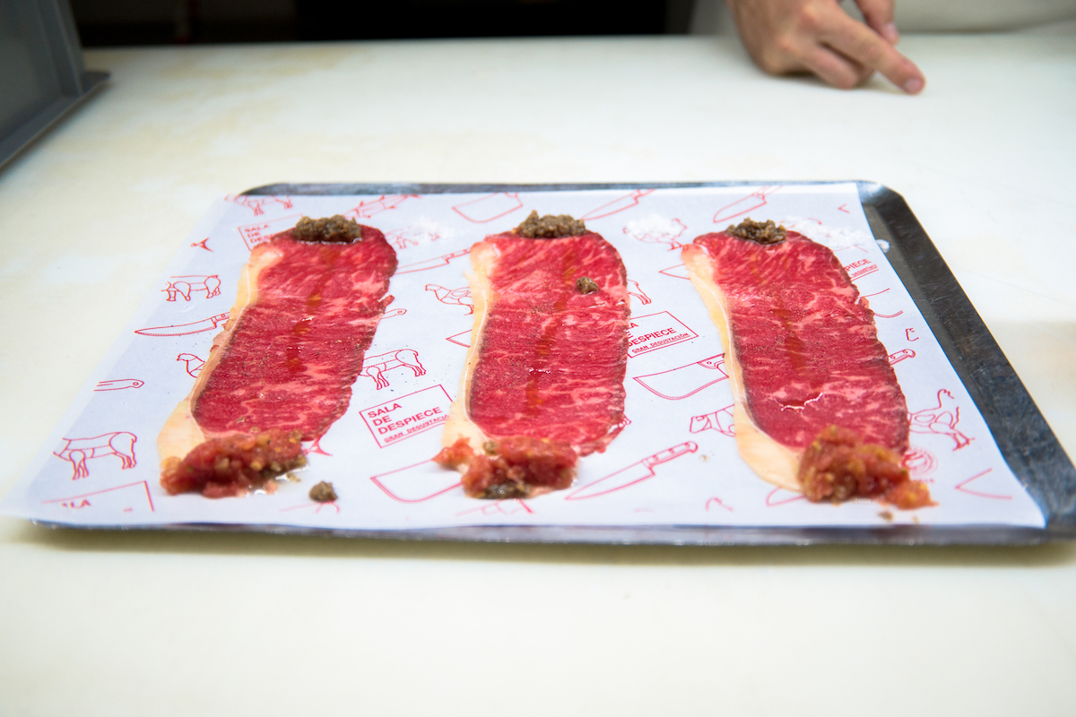 Tres lonchas de carne cortadas muy finas en una bandeja blanca con trocitos de salsa y condimentos en cada extremo.