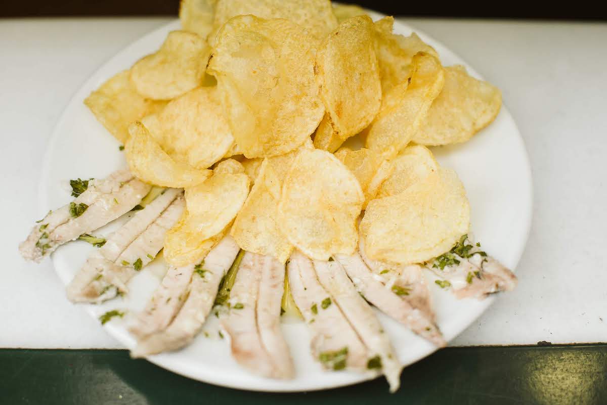 Plano cenital de anchoas blancas marinadas en vinagre y hierbas delante de un montón de patatas fritas en un plato blanco