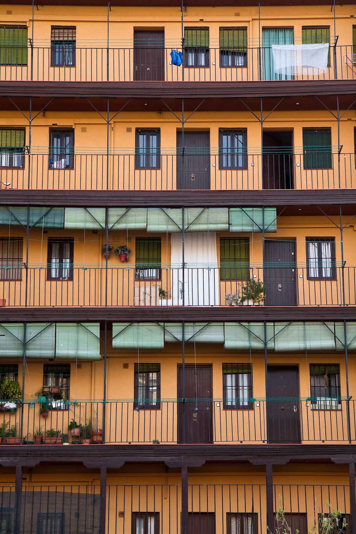 Vista exterior de cinco plantas de un bloque de apartamentos con balcones y persianas verdes.