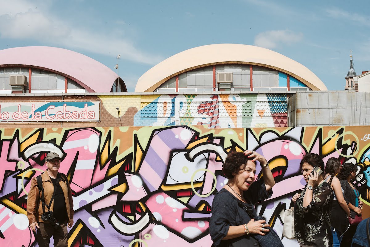 Gente caminando delante de un colorido mural de arte callejero en las paredes exteriores de un gran edificio del mercado.
