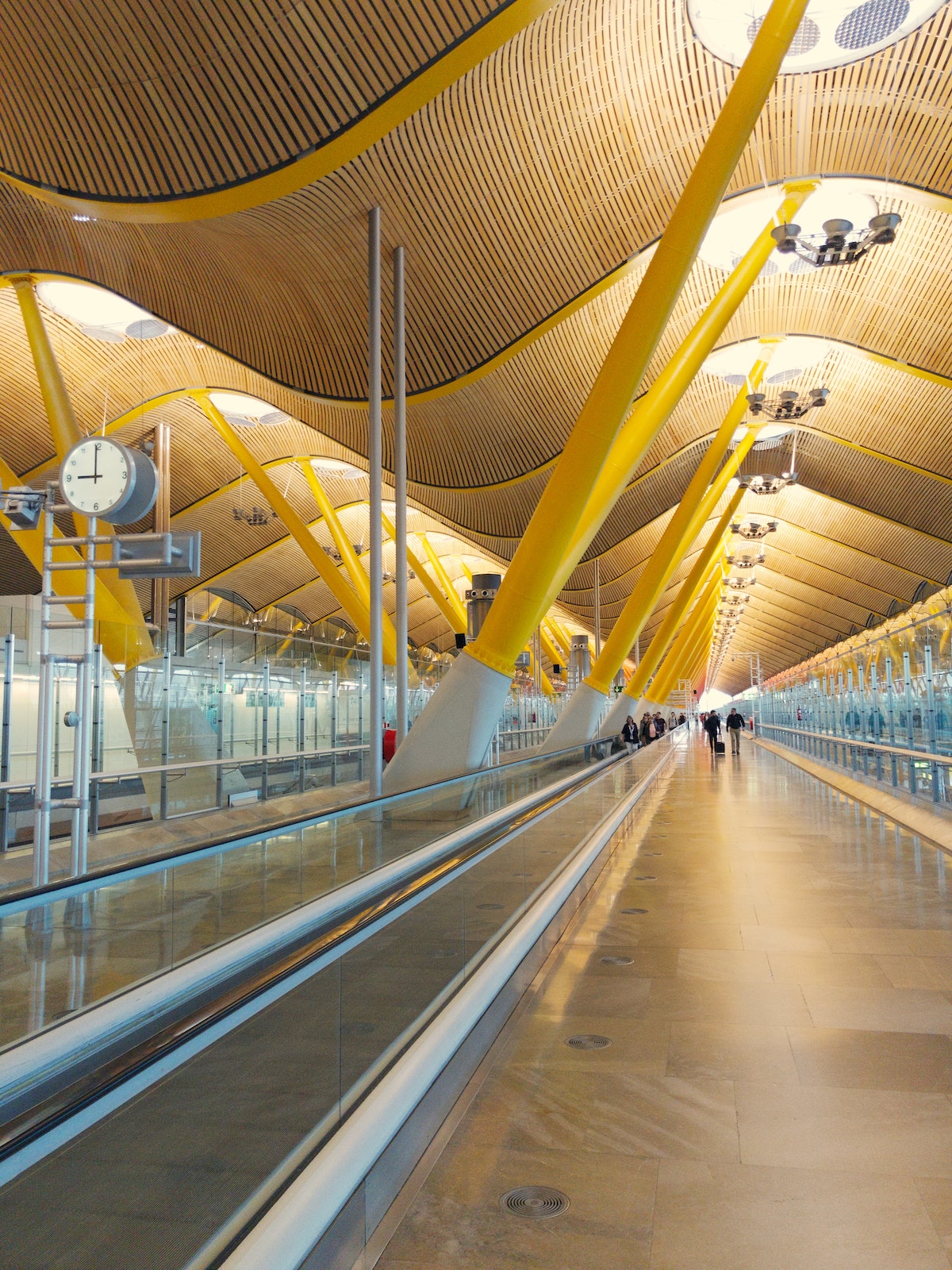 Interior de un aeropuerto con una pasarela móvil y un moderno techo ondulado sostenido por vigas amarillas.